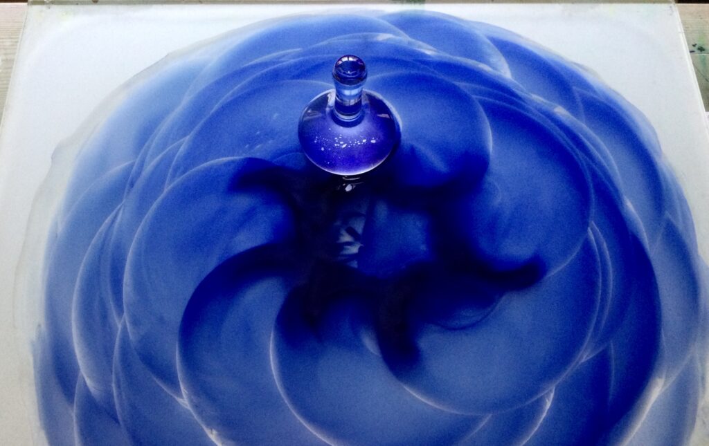 Image shows number one of three favourite tools to make watercolour paint. The glass muller sits on top of the glass slab with swirls of blue paint.